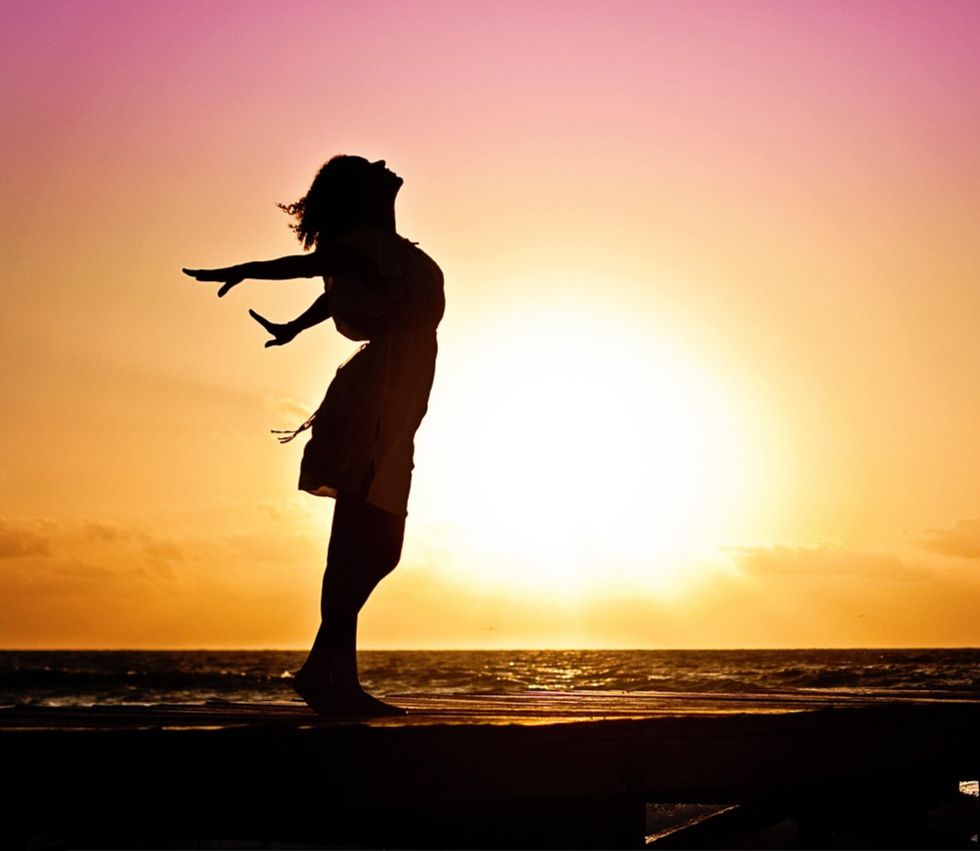 femme qui retrouve sa respiration, son énergie femme qui ouvre ses bras au coucher de soleil en bord de mer